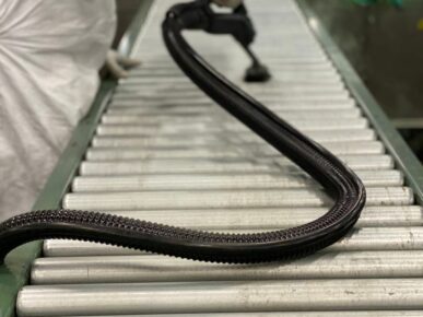 PCT Janitorial - Professional cleaner vacuuming conveyor belt in industrial facility.